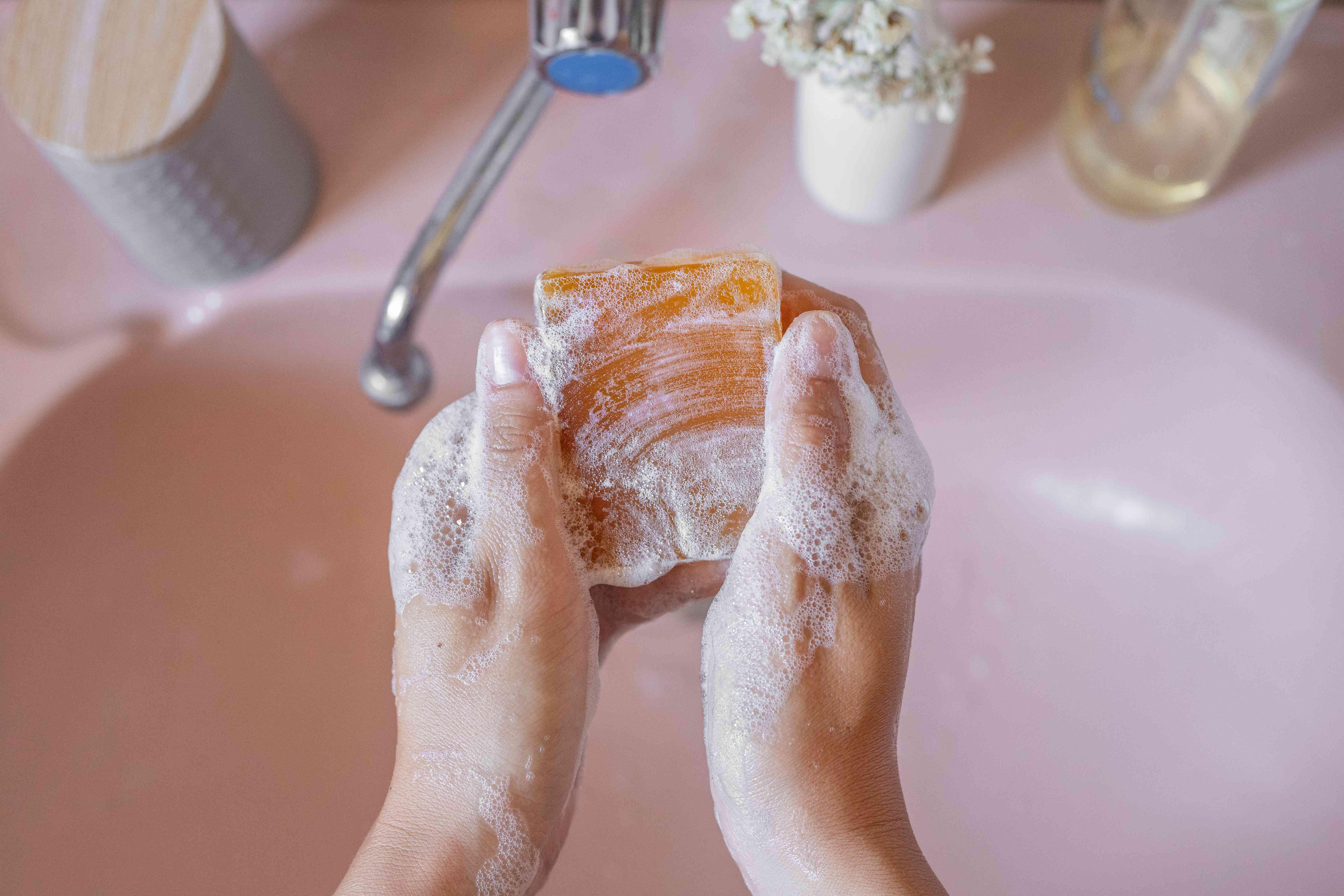 一名女子在浴室的粉色水槽中用天然肥皂洗手