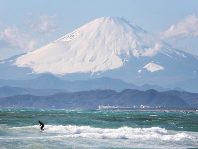白雪覆盖的富士山后面的距离较小的山和冲浪者在蓝绿色的水