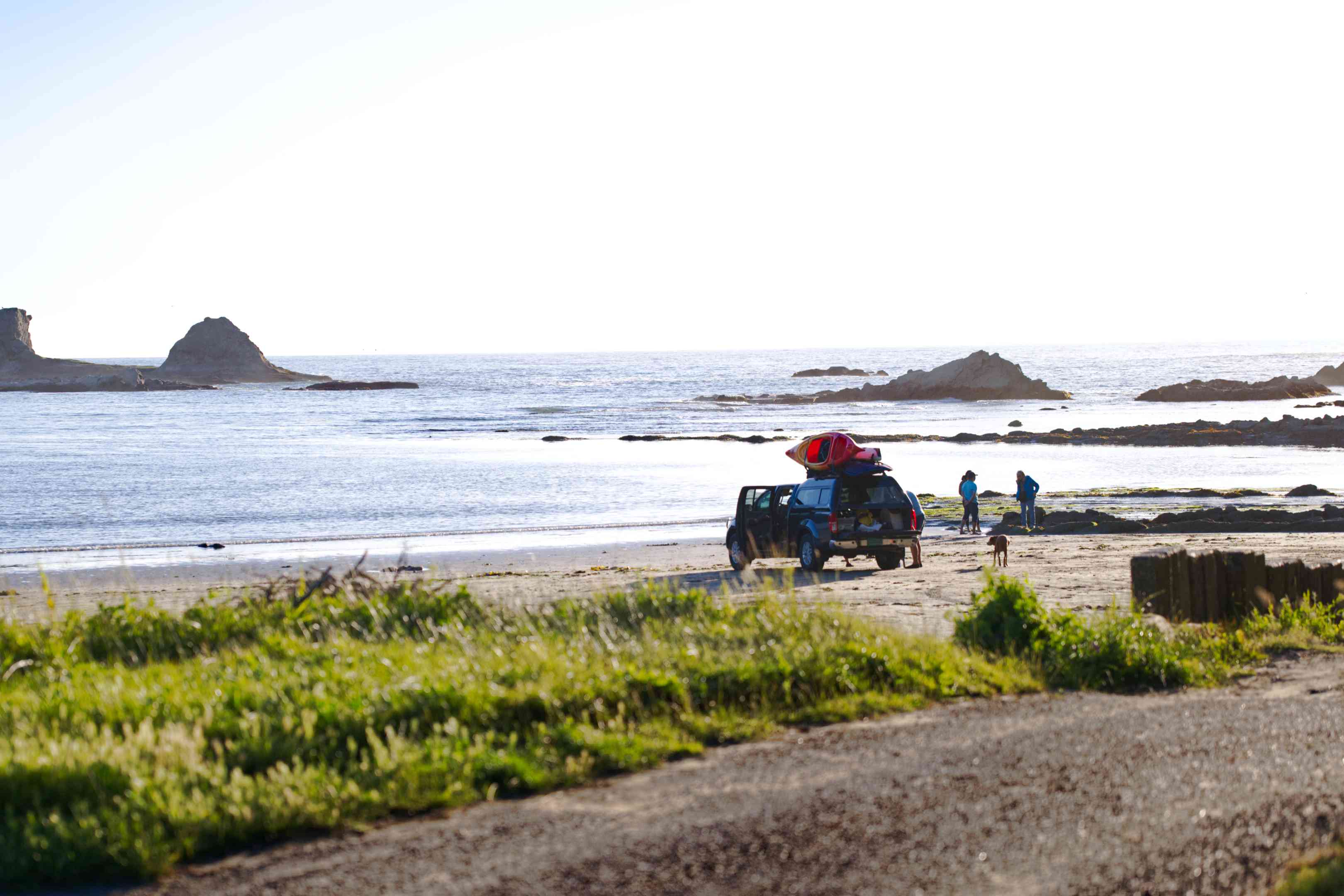 顶部有独木舟的SUV停在岩石海滩上，准备野营