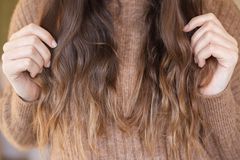 女人穿着毛衣，带有波浪状的长棕色头发，手指穿过末端