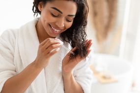非裔美国妇女在家里的现代浴室中使用血清对受损的干头发。