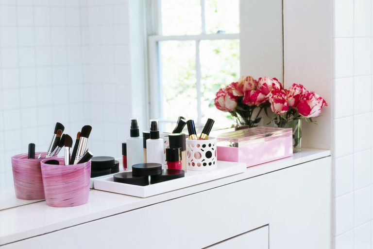 化妆品放在浴室窗台上的粉色容器里，角落里放着一瓶粉色郁金香