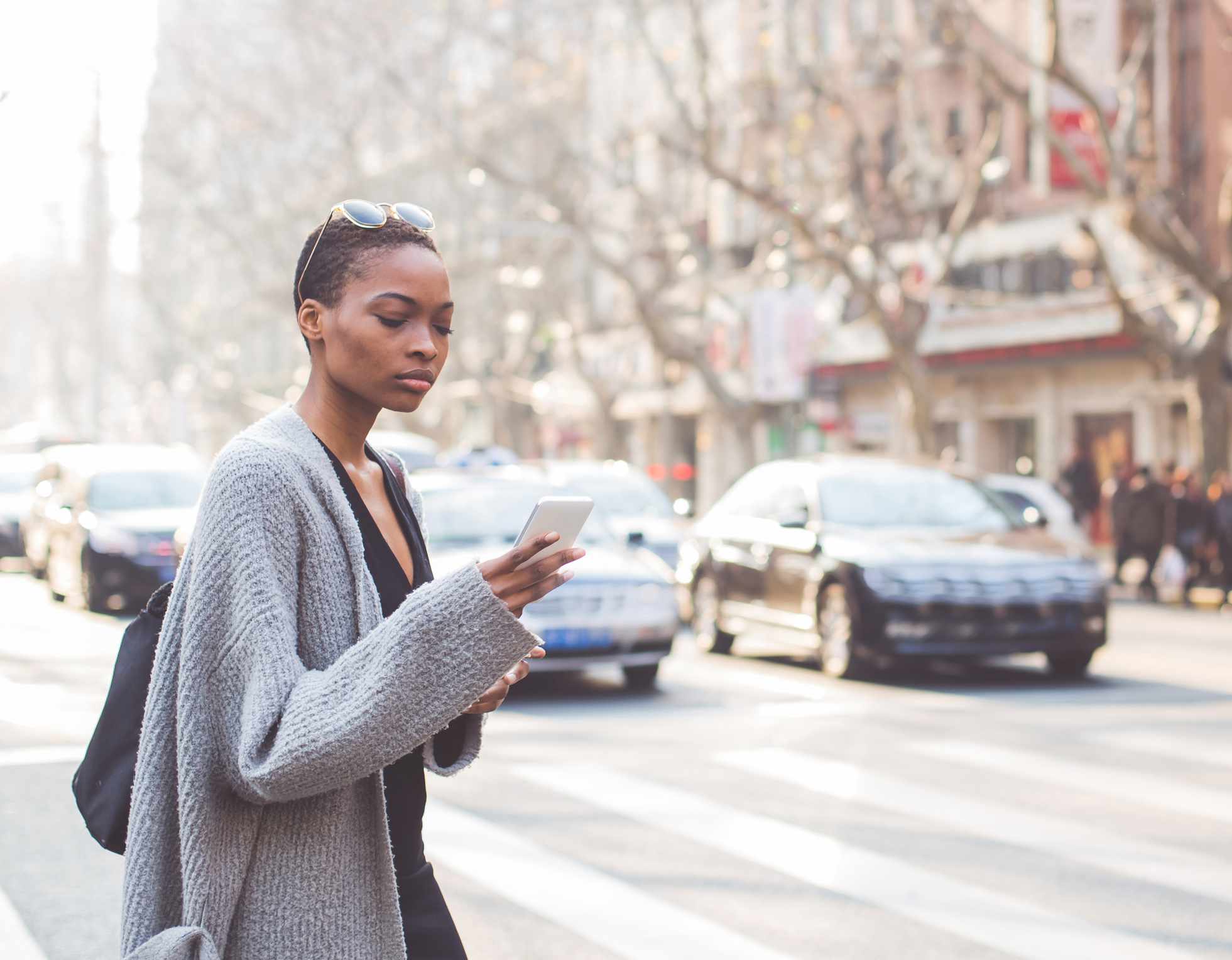一个年轻的黑人妇女看着她的手机穿过马路。