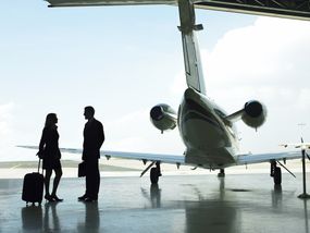 一对富有的夫妇拿着行李站在私人飞机前的机场衣架上