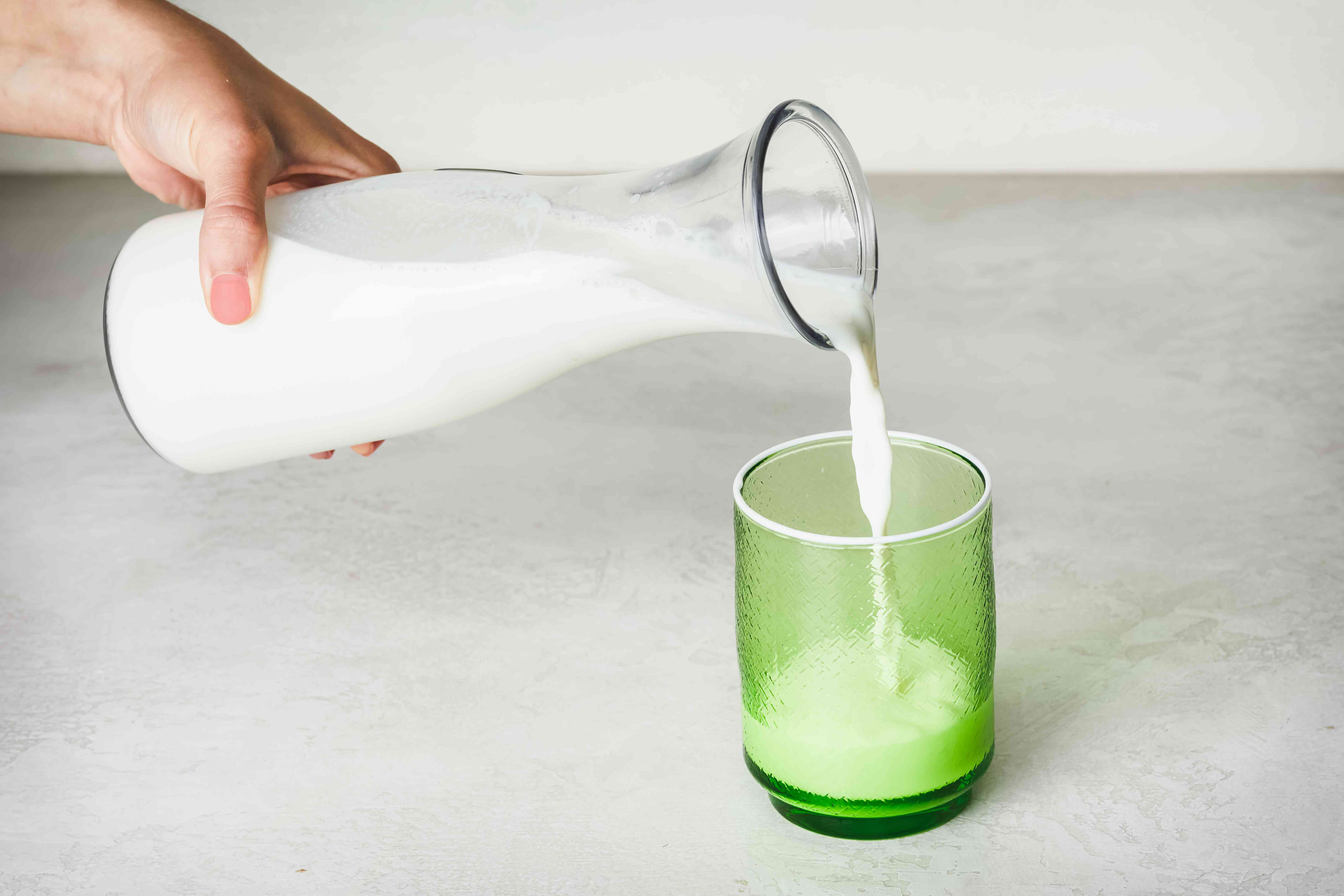 手倒玻璃壶全脂牛奶为绿色玻璃杯子