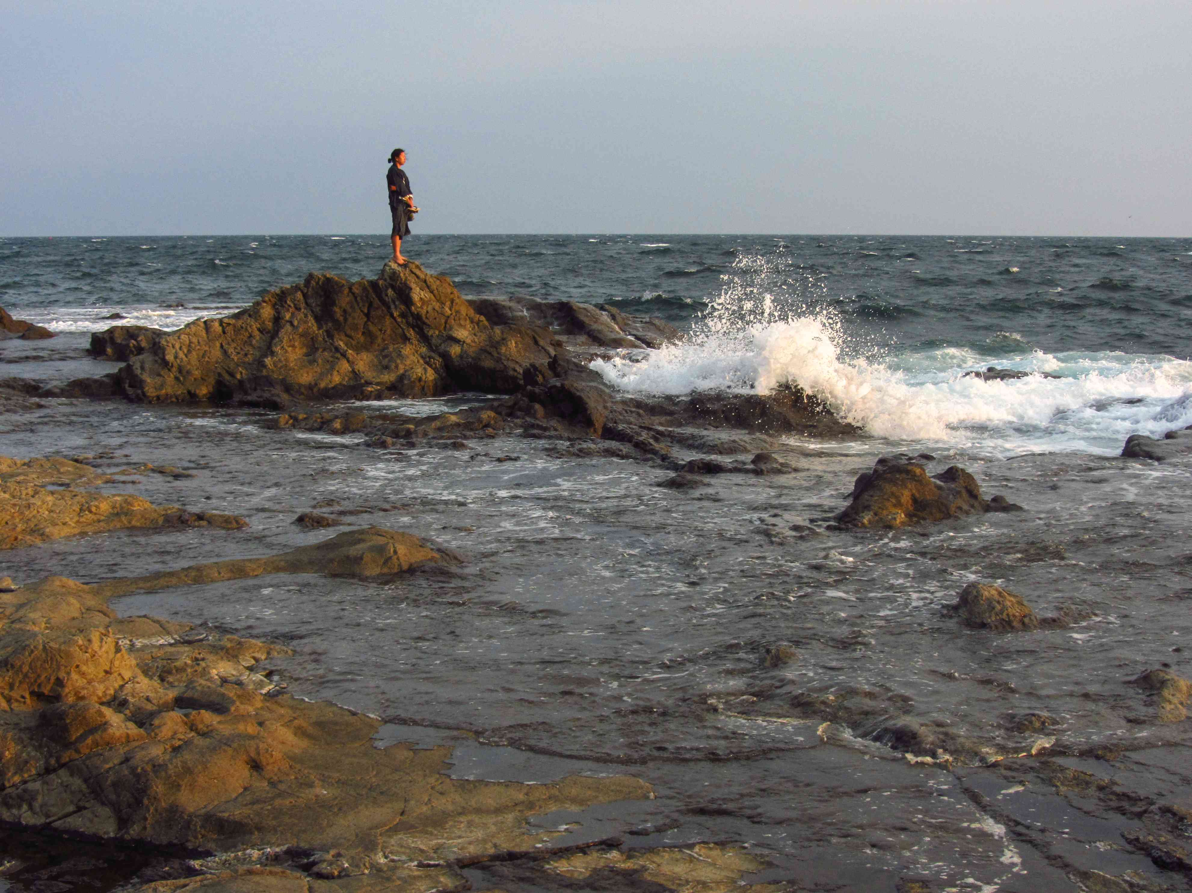 一个人独自站在崎岖的岩石上，海浪在他们周围拍打