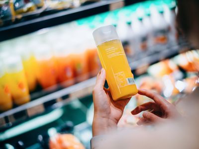 横跨亚洲年轻妇女超市杂货购物取新橙汁瓶上营养标签