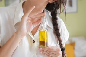 woman holds almond oil bottle with long brown braided hair