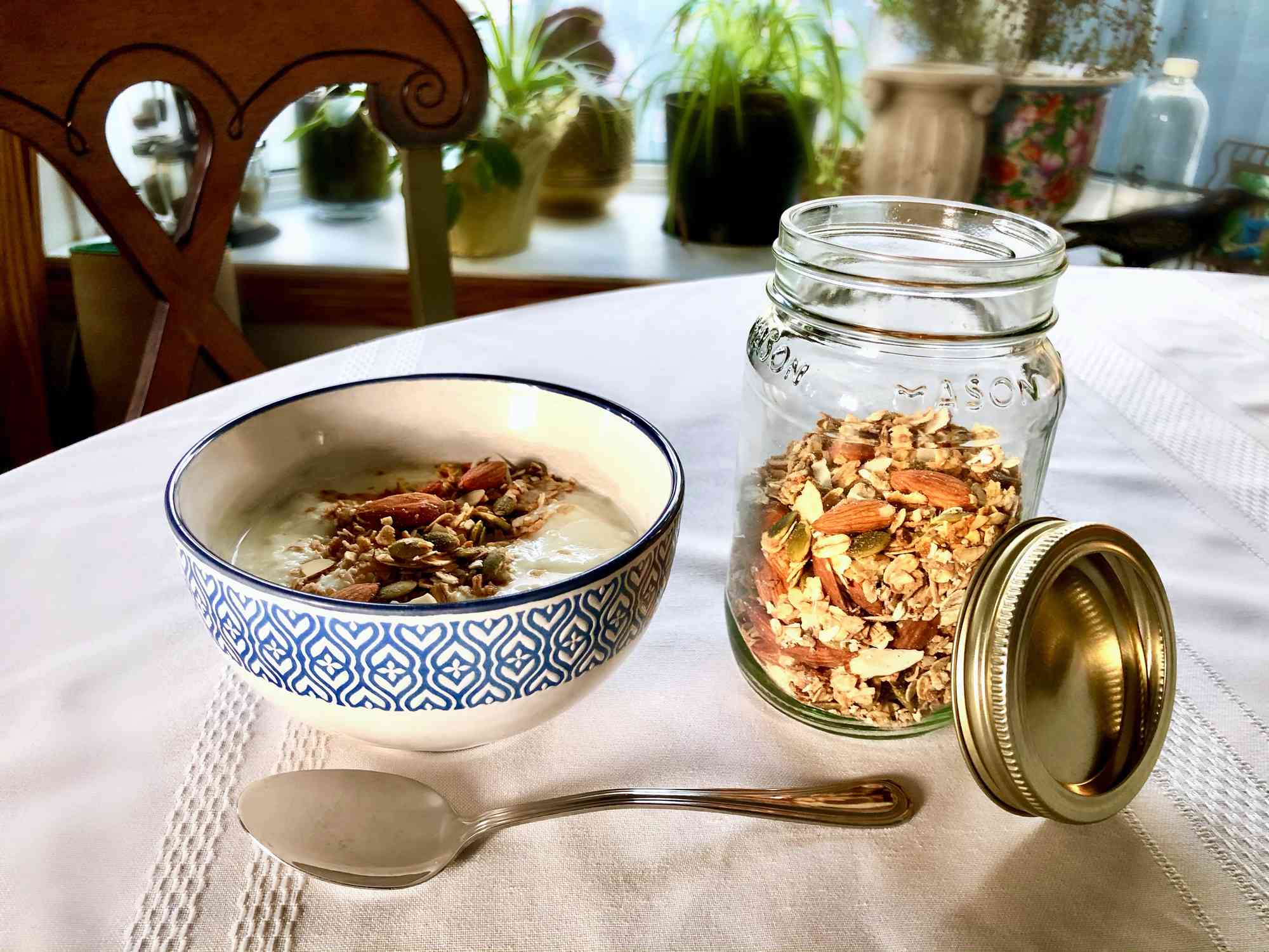 格兰诺拉麦片装在一个玻璃瓶里，放在桌子上的碗和勺子旁边。