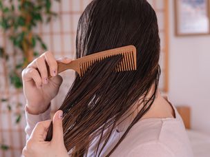 侧面拍摄的女人梳理湿棕色头发与棕色梳子