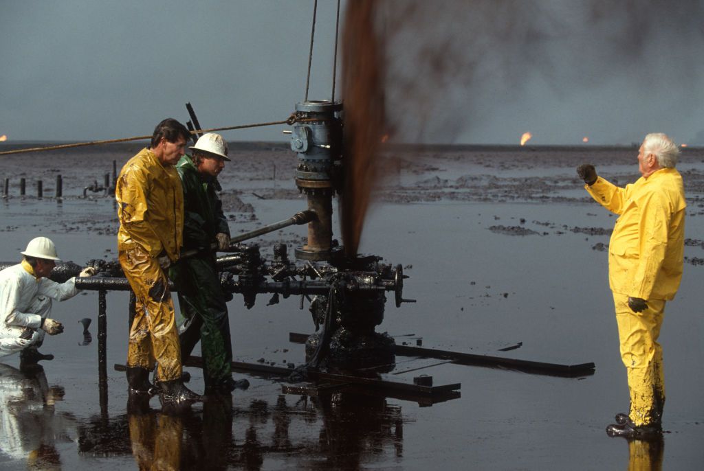 1991年的科威特，海湾战争期间，石油工人在井喷中封堵油井。其他油井在幕后燃烧。