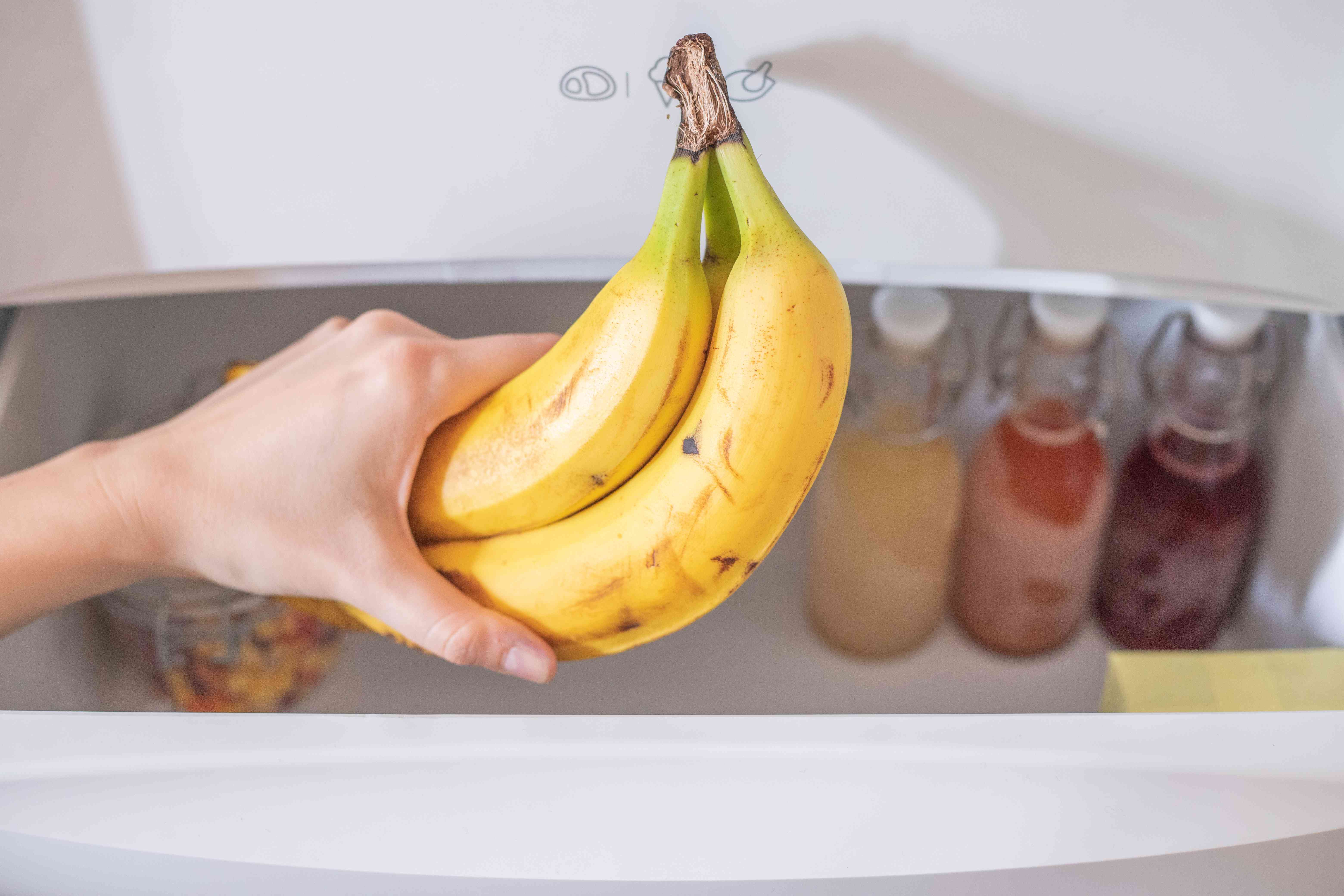手拿一堆香蕉在冰箱打开抽屉与其他冷冻食品