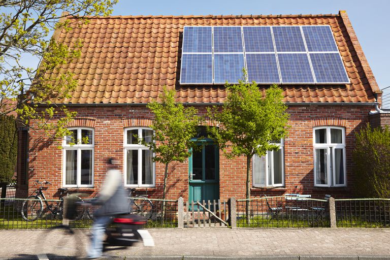 在装有太阳能电池板的房子前骑自行车的人＂class=
