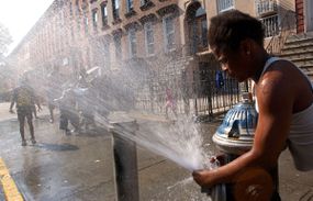 一个女孩将喷雾从一个开放的消防栓喷射，因为孩子们在纽约市布鲁克林省的布鲁克林省的夏季加热中冷却。“width=