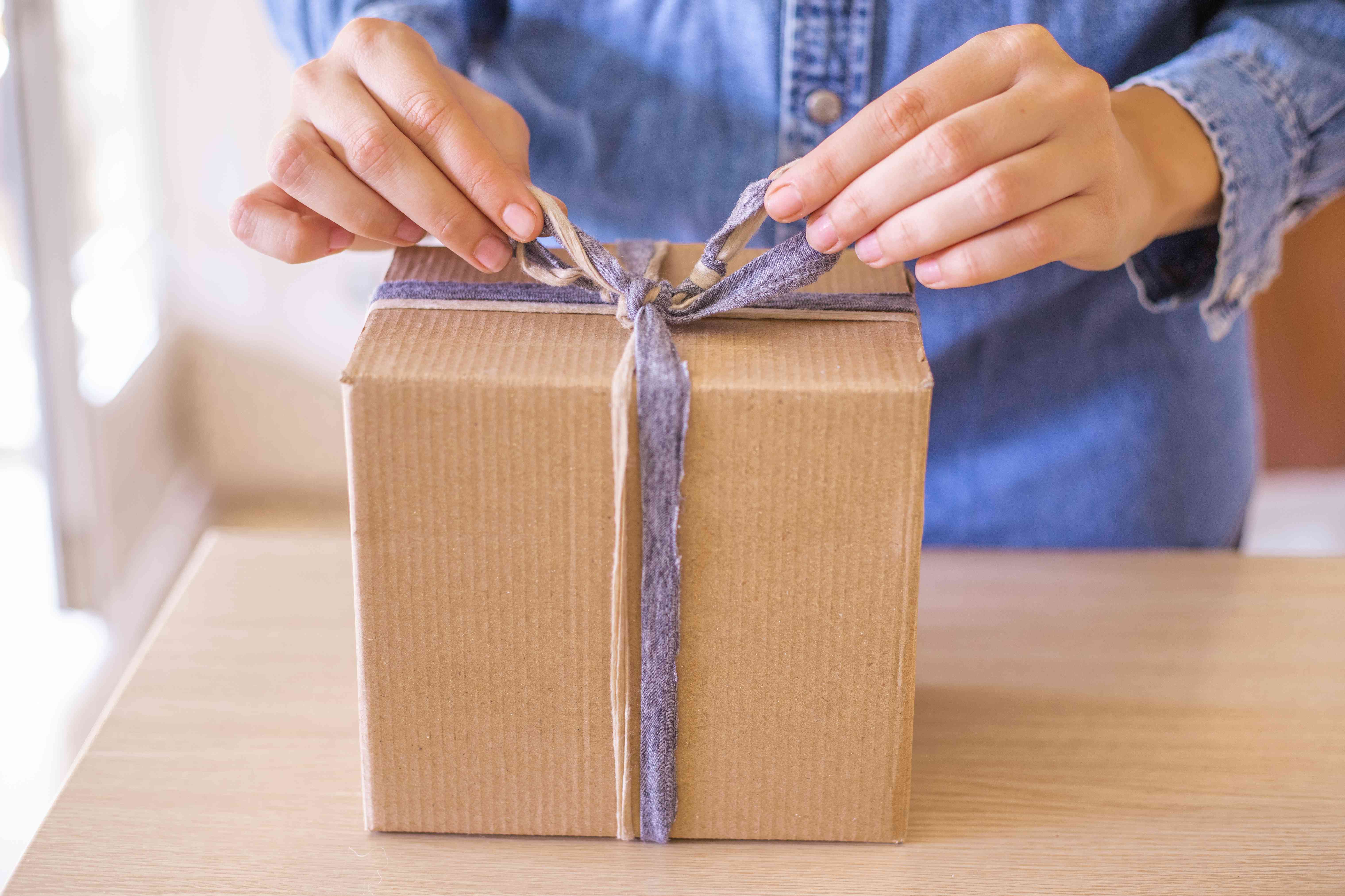 女人在牛仔衬衫领带蝴蝶结与剩余的织物碎片在包装盒的礼物＂width=