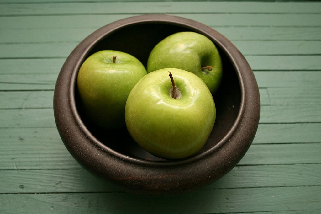 一个木桌上放着三个苹果的碗”width=