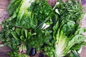 一堆绿叶蔬菜，包括芝麻菜，罗马毛，香菜，绿洋葱等等“width=