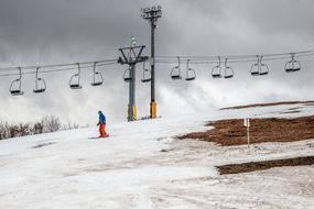 一个人在滑雪场滑过空荡荡的升降椅和一片草地，因为缺少雪，滑雪场不得不关闭一些斜坡，