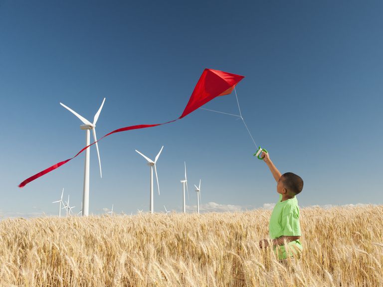 一个小男孩在放风筝和风力涡轮机。”class=