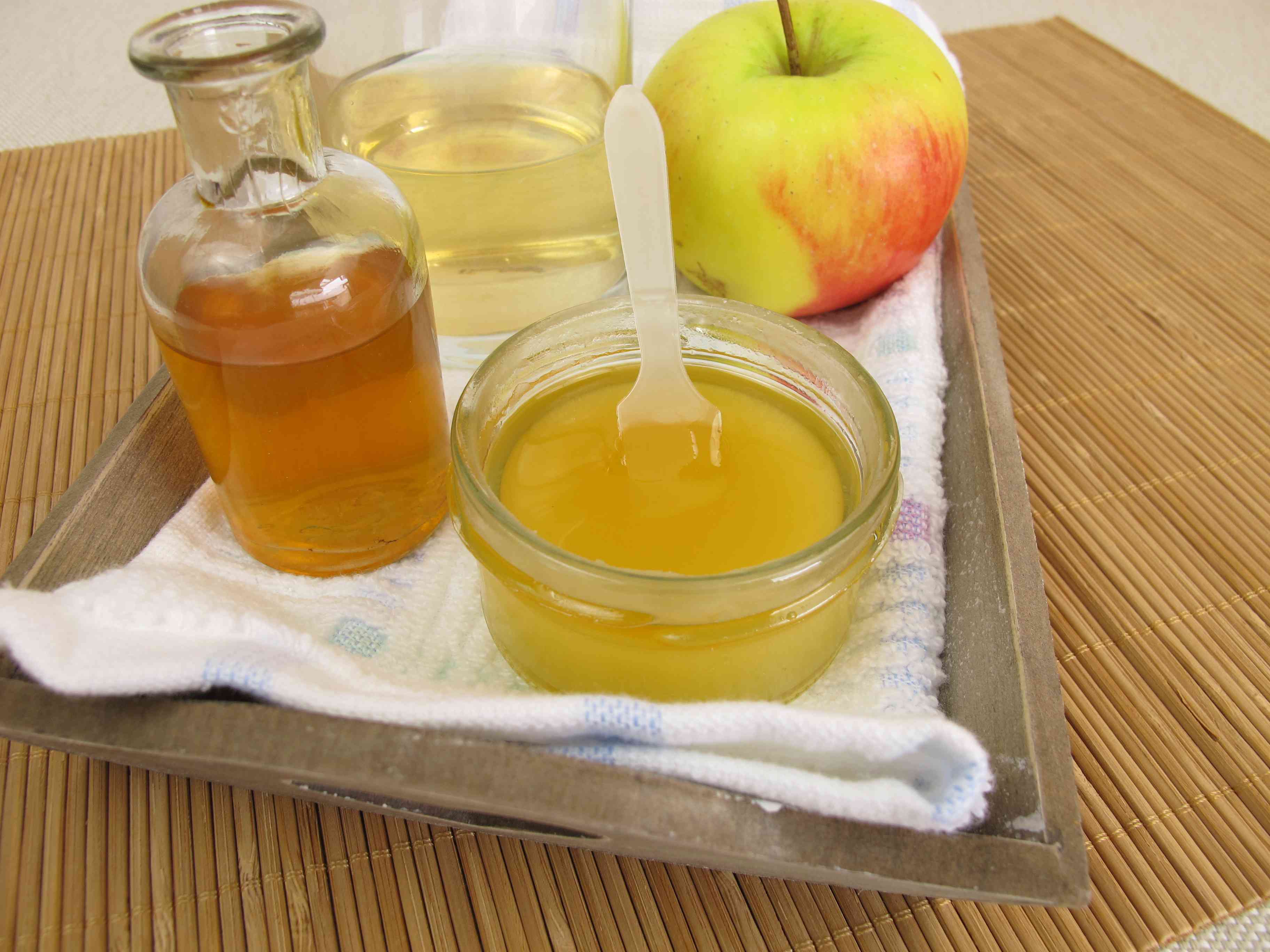 一碗苹果醋与水混合在一瓶苹果醋和背景中的苹果旁边“width=