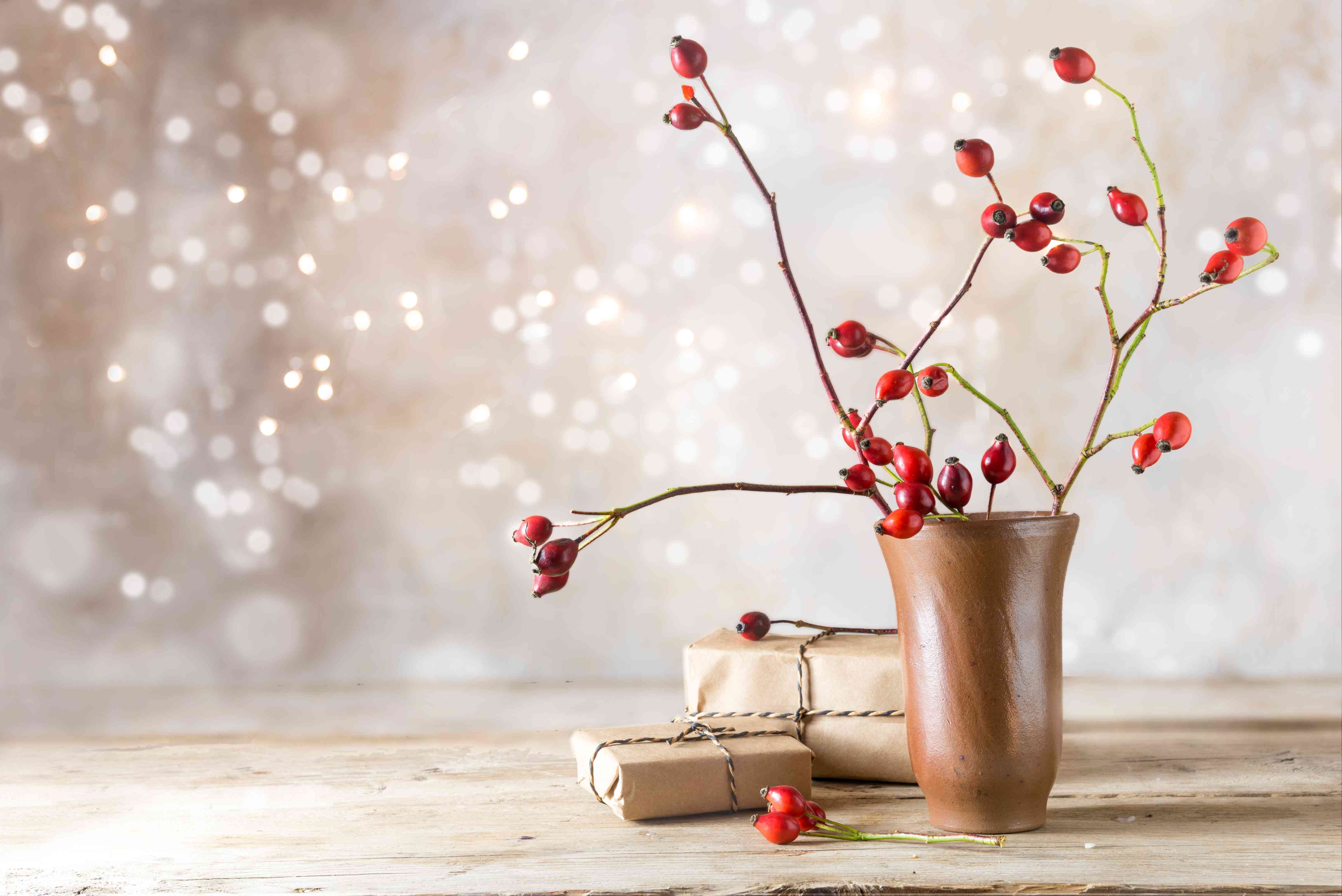 小礼物包裹和玫瑰果分支在乡村木桌上反对复古与模糊散景墙灯,秋天或圣诞节装饰与复制空间”width=