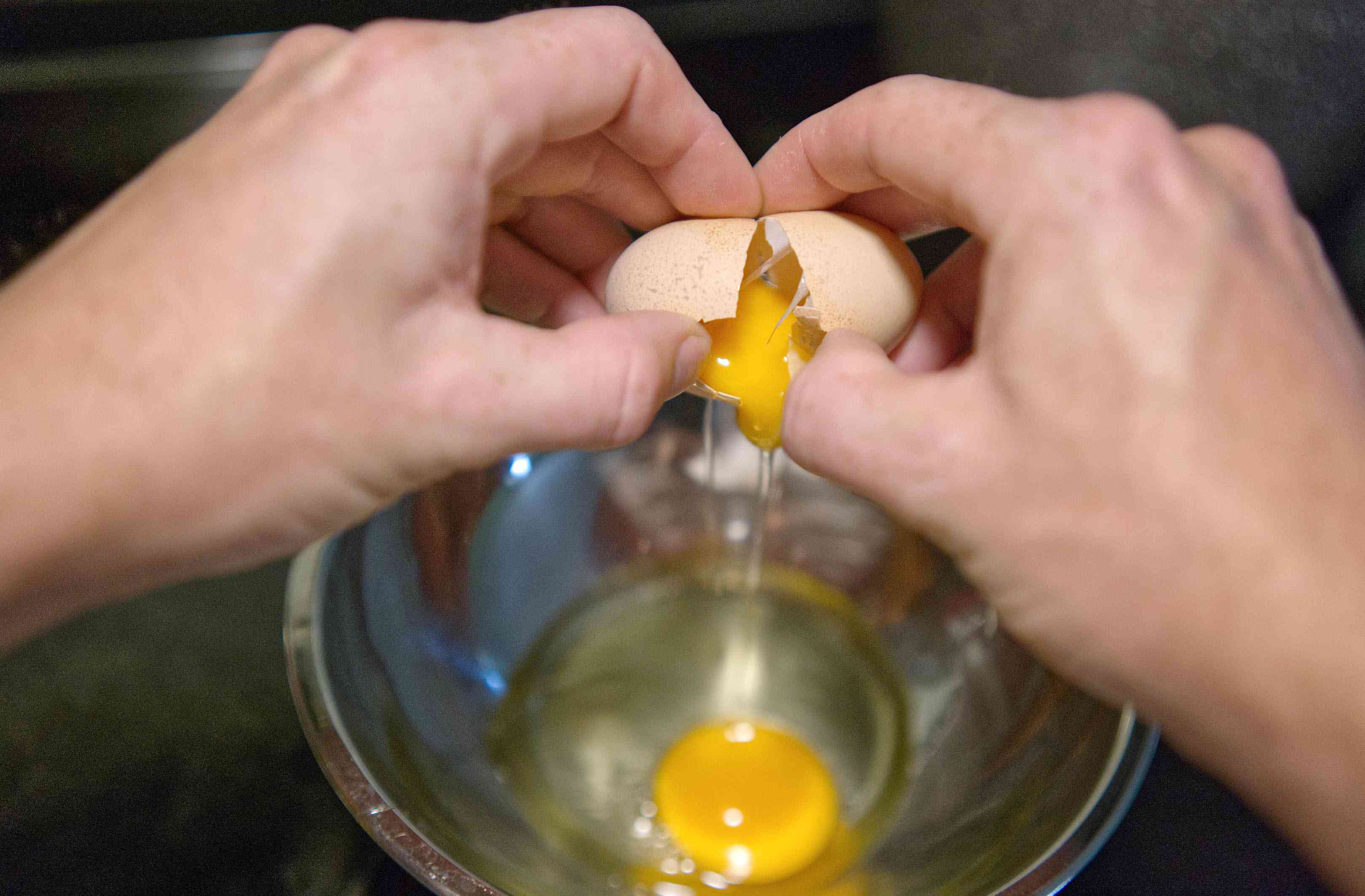 两只手把鸡蛋敲进钢碗里检查新鲜程度