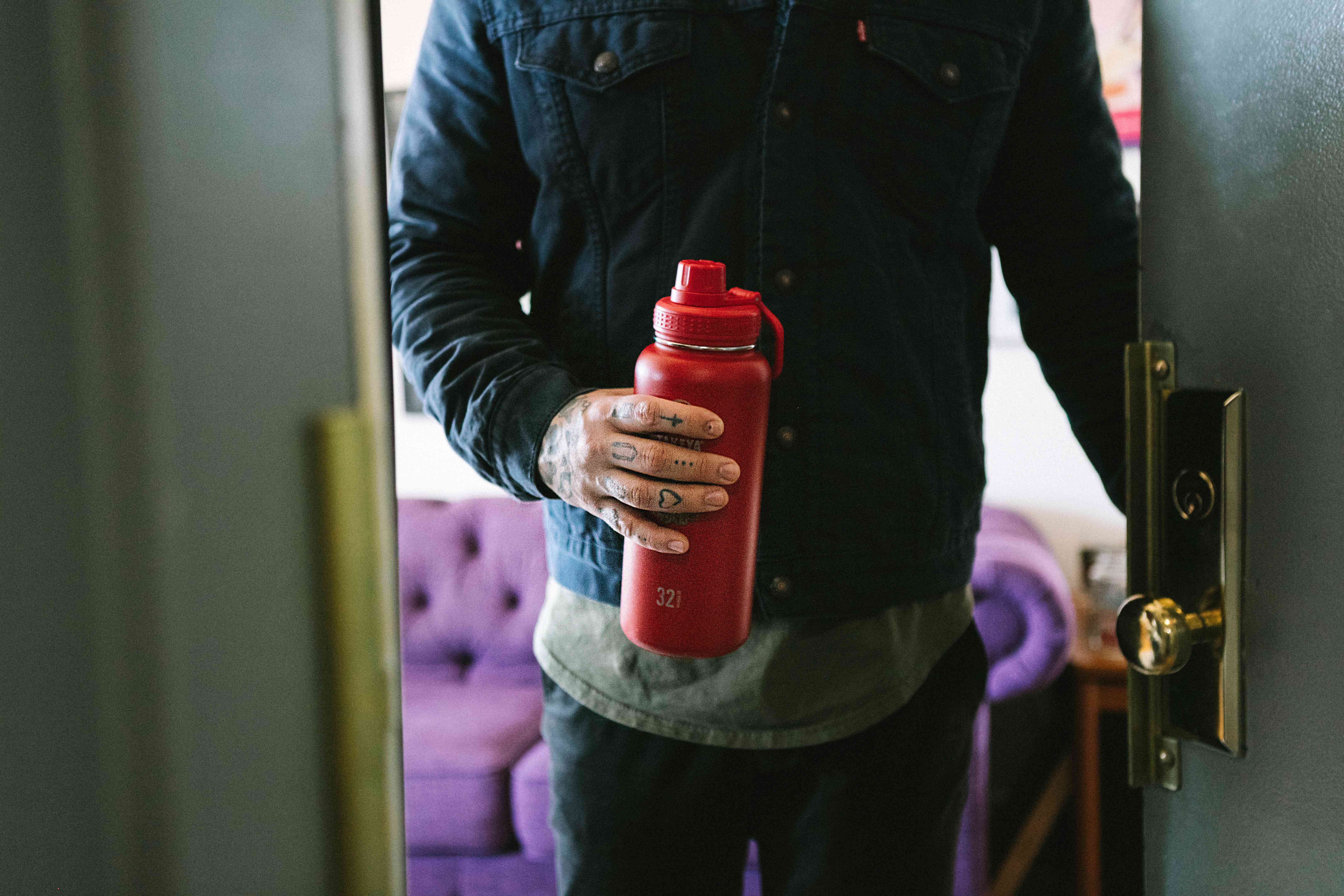 Alt人员打开公寓门，手里有红色可重复使用的热水瓶咖啡容器