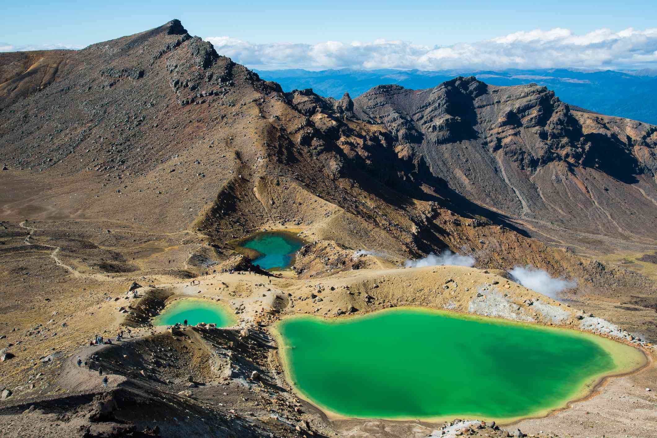 在汤加里罗高山渡口，一个大的和两个小的翠绿色的湖泊被群山环绕，有明亮的蓝色海水、蓝天和远处低垂的白云