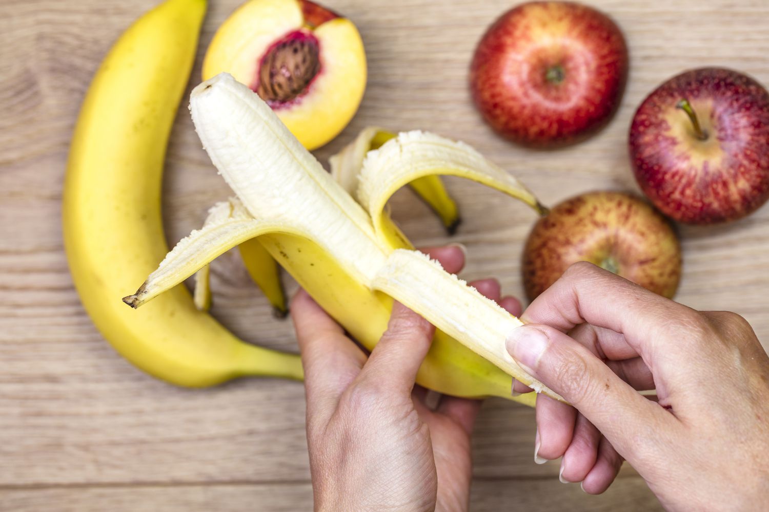 一只手剥一根香蕉苹果和桃子。
