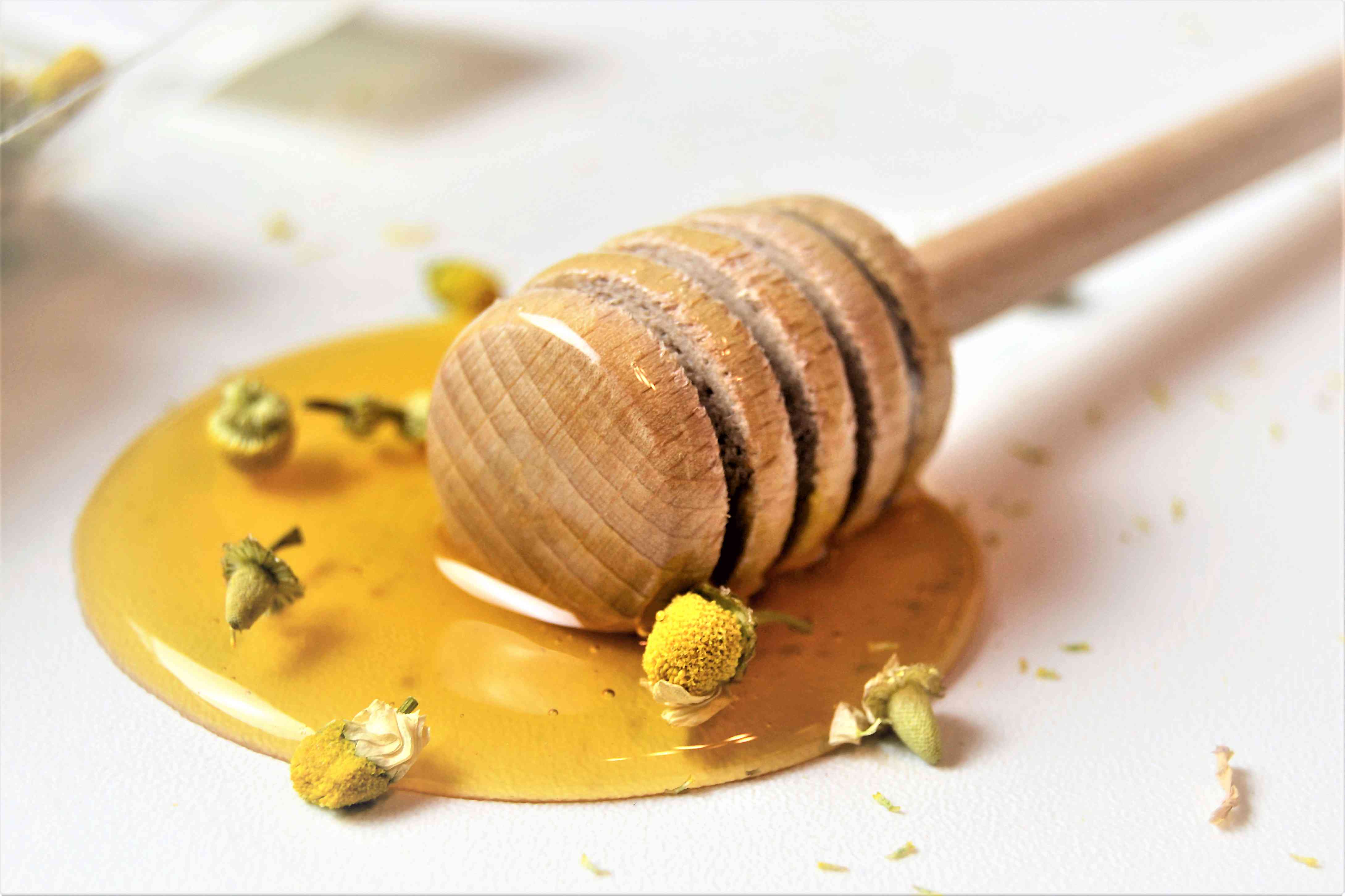 蜂蜜与蜂蜜勺与甘菊茶花作为背景，特写
