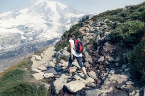 徒步旅行者在岩石小径上行走，雷尼尔山（Mount Rainier）在背景中“width=