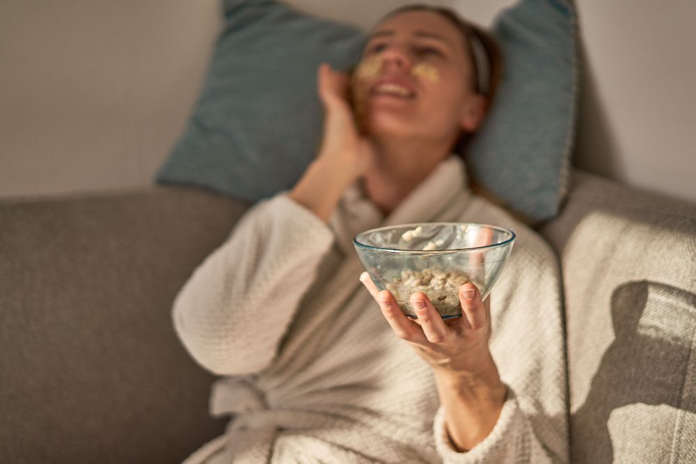 女子斜靠在枕头上，拿着玻璃碗装满自制燕麦面膜