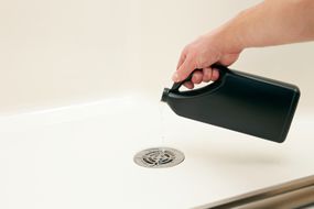 用液体排水管清洁剂清理淋浴间“一名男性正在把液体排水管清洁剂倒入淋浴间的排水管中，以溶解堵塞，改善水流。或者，这张照片也可以用来把废物从下水道里倒下去。”