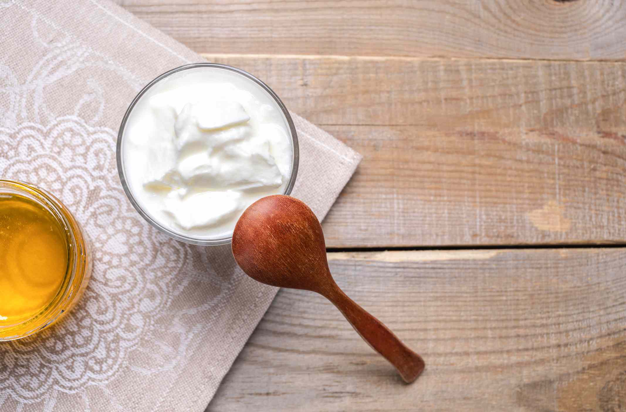 一杯浓稠的自制酸奶，木勺和一罐蜂蜜，放在亚麻图案的餐巾上，放在质朴的木桌上