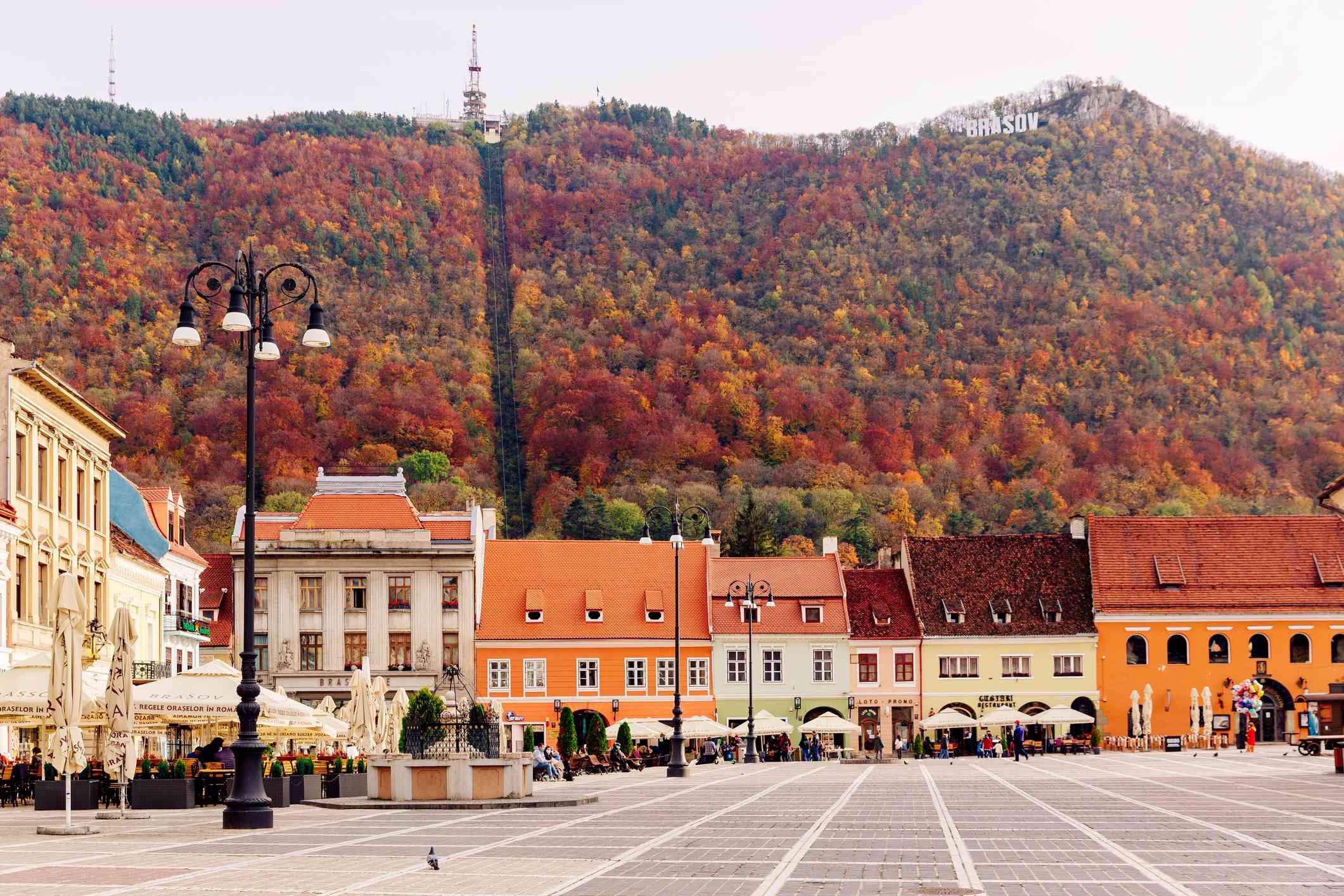 位于罗马尼亚布拉索夫的Piata Sfatului广场的两层建筑，色彩鲜艳的橙色、黄色和粉色，背景是被秋天颜色的树木覆盖的小山