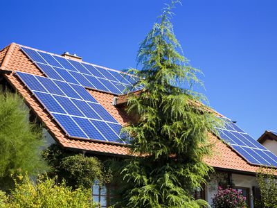 房子急剧倾斜的赤褐色的屋顶覆盖着太阳能电池板的数组与树木和灌木环绕它