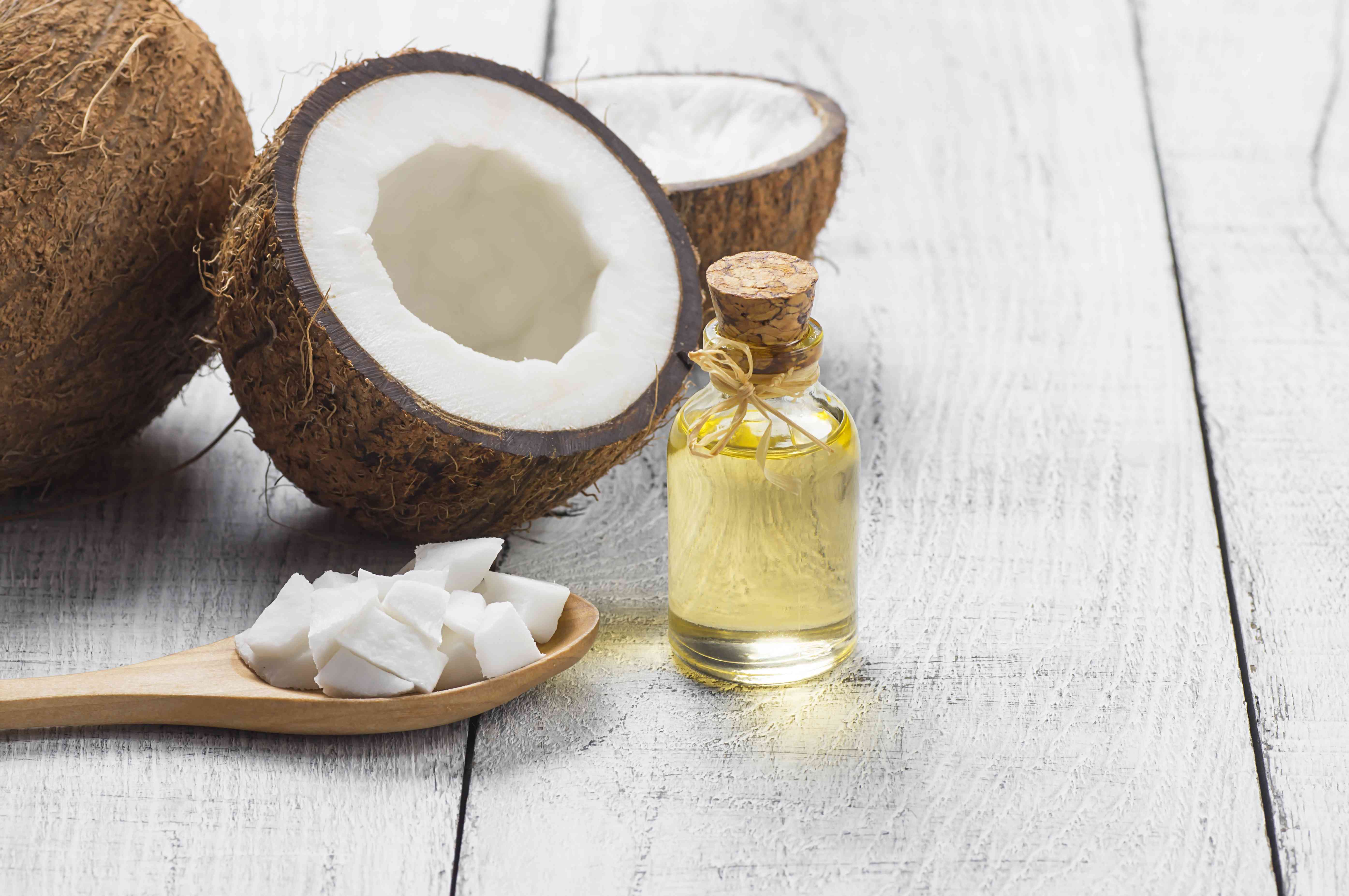 玻璃瓶的椰子油与新鲜的椰子水果在乡村背景，替代治疗医学概念，椰树