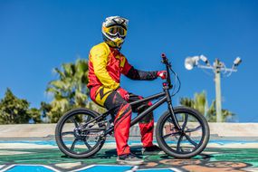 身穿彩色西装、戴着护目镜和头盔的人，坐在由Life electric Vehicles公司制造的电动BMX自行车上