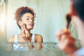 一个女人在镜子里用化妆刷＂width=