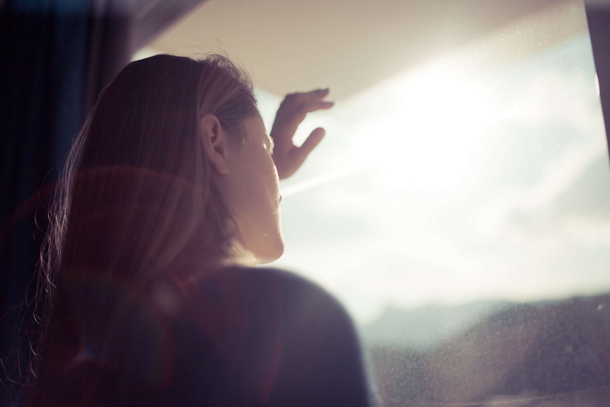 一个女人透过窗户看，阳光照进来。＂width=