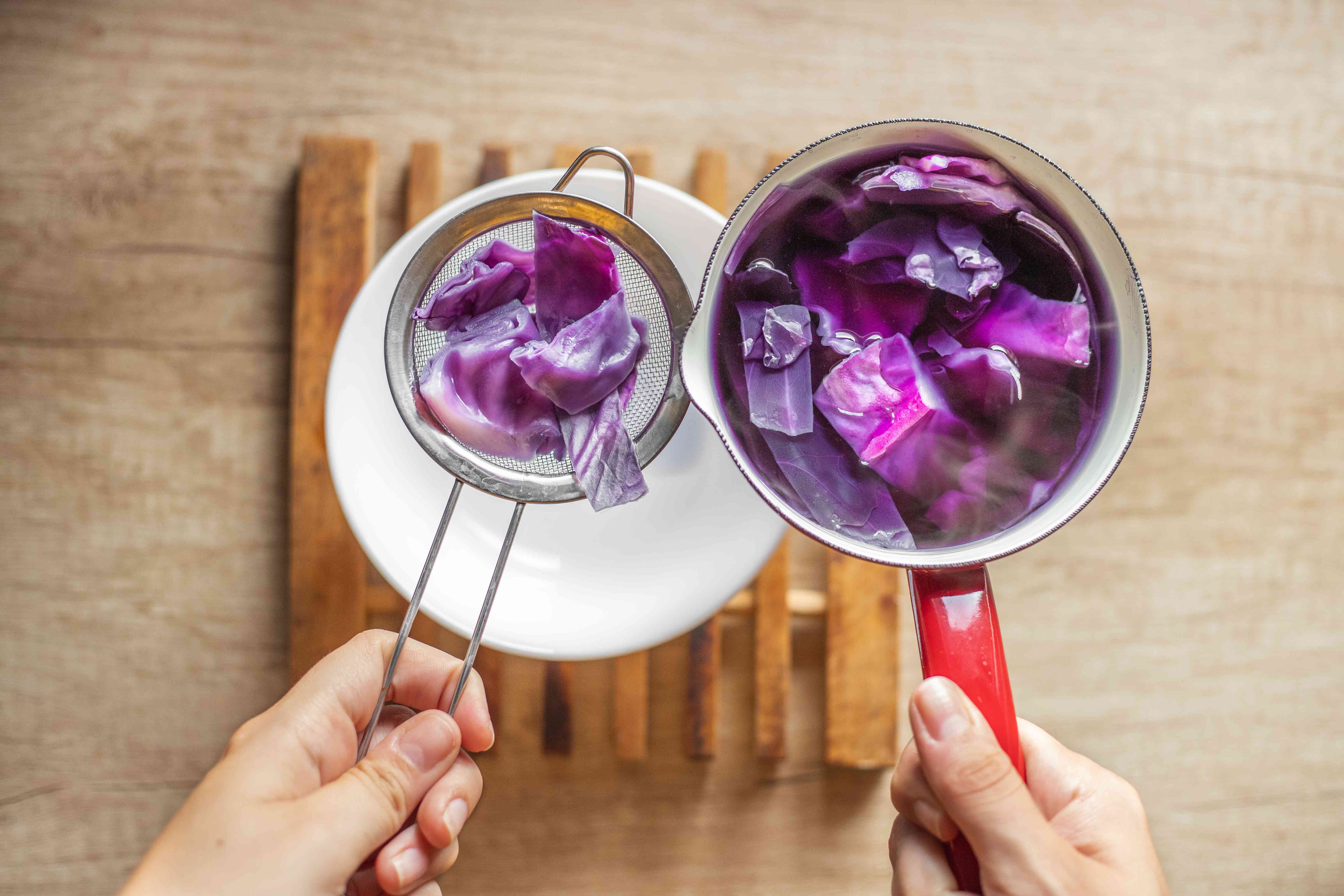 用一个筛子把红卷心菜从沸腾的紫色水中滤出，放进碗里＂width=