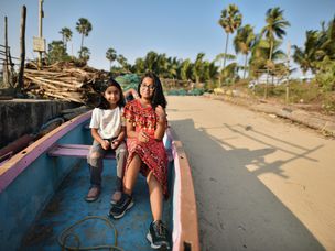 两个小女孩坐在印度乡村海岸线上的一艘渔船上