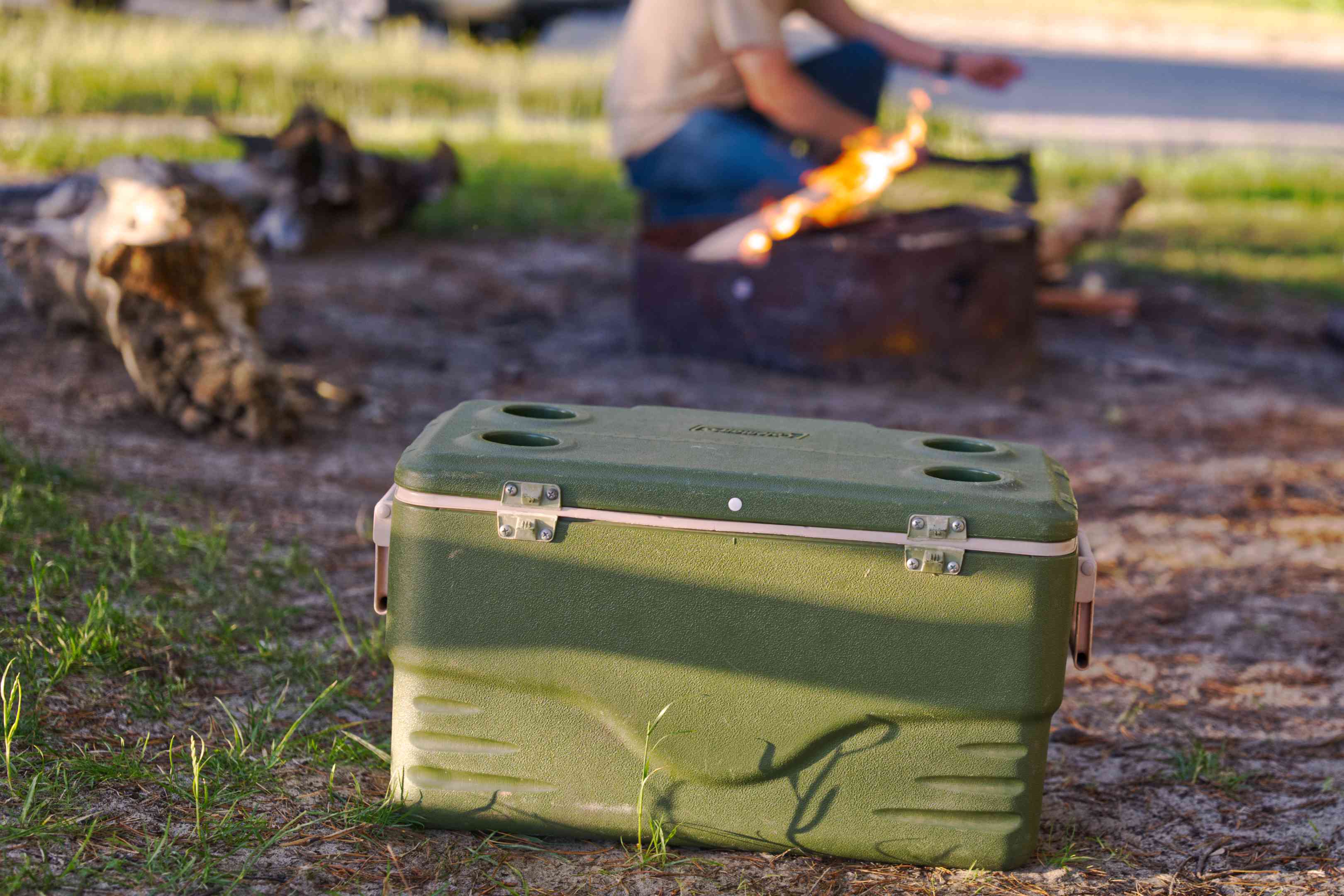 陆军绿塑料冷却器坐在肮脏的家伙使火在营地firepit