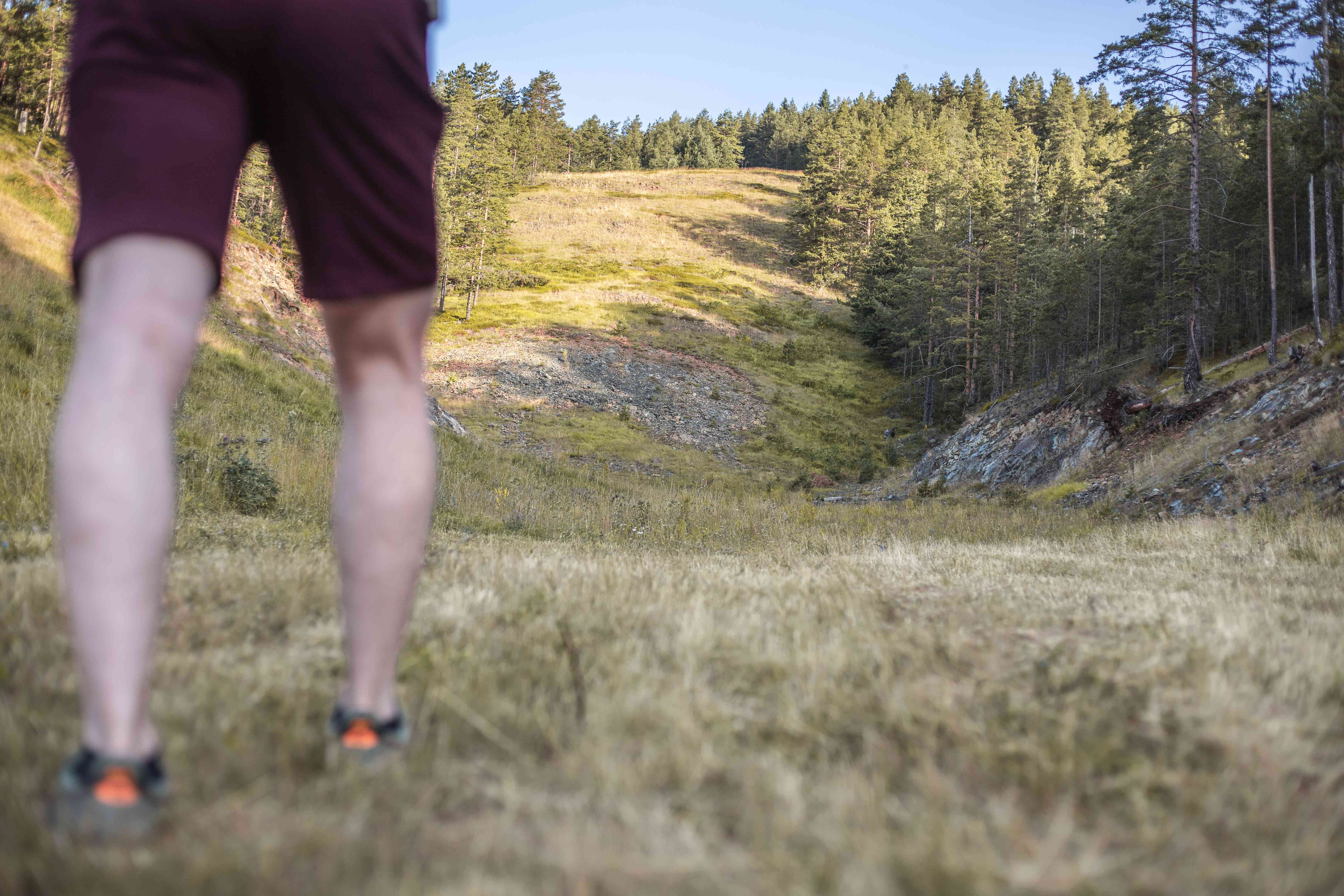 穿着短裤的家伙准备在树木繁茂的岩石山上陡峭的斜坡上行走