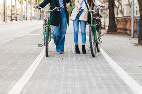 一对穿着牛仔裤的时髦夫妇在城市街道上骑着绿色自行车