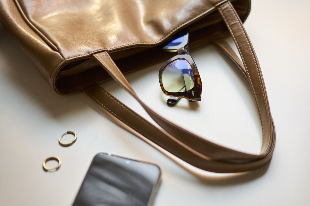 太阳镜和手机旁边是棕色皮革钱包，用于包装“width=