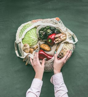 女性的手拿着环保的网状购物袋和蔬菜