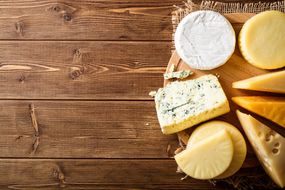 各种各样的奶酪放在木板上＂width=