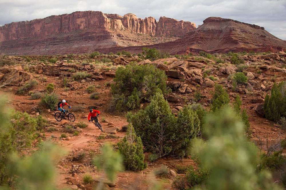两个山地自行车手在犹他州沙漠的一条小路上绕过一个急转弯