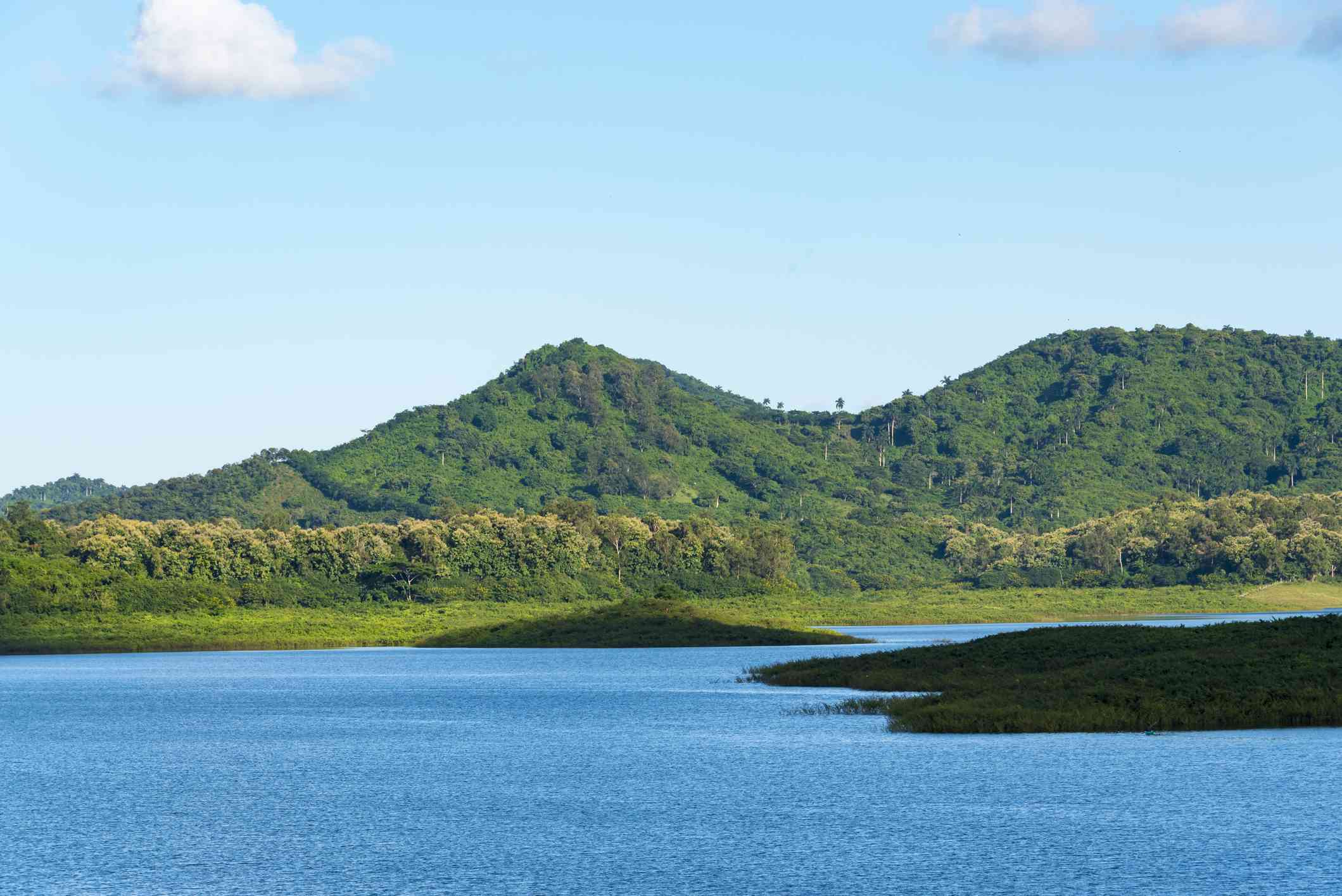 Hanabanilla湖的充满活力的蓝色覆盖着低绿色叶子与豪华的绿色覆盖的escambray山脉在距离的蓝天与光，白色云盖子下